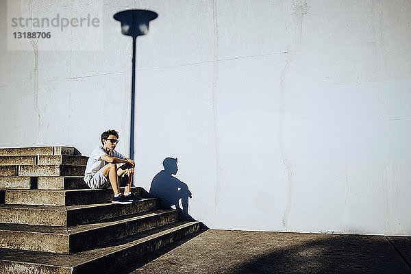 Junger männlicher Läufer  der sich auf einer sonnigen städtischen Treppe ausruht