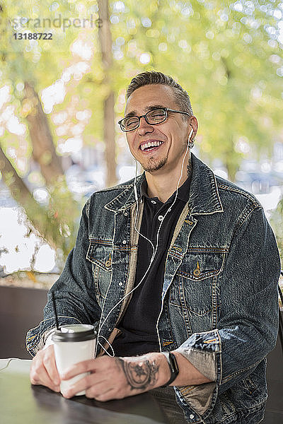 Lachender Mann trinkt Kaffee und hört Musik in einem Cafe