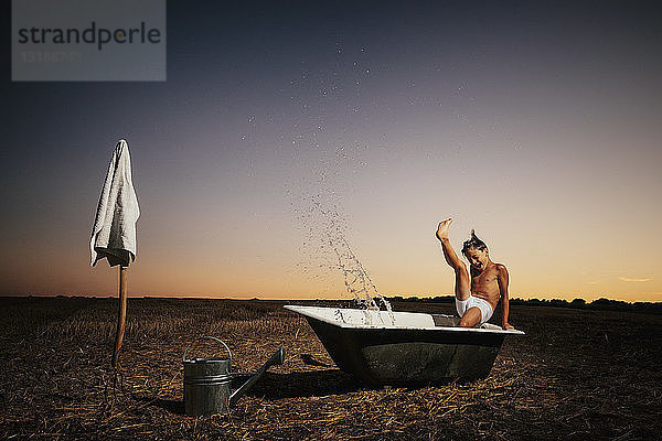 Junge  der in einer Badewanne in einem ländlichen Feld bei Sonnenuntergang plantscht