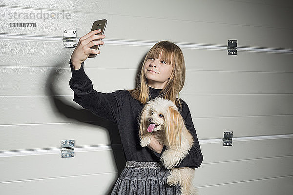 Mädchen mit Hund macht Selfie mit Fotohandy in Garage