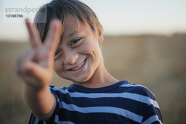 Porträt lächelnder  unbekümmerter Junge  der das Friedenszeichen macht