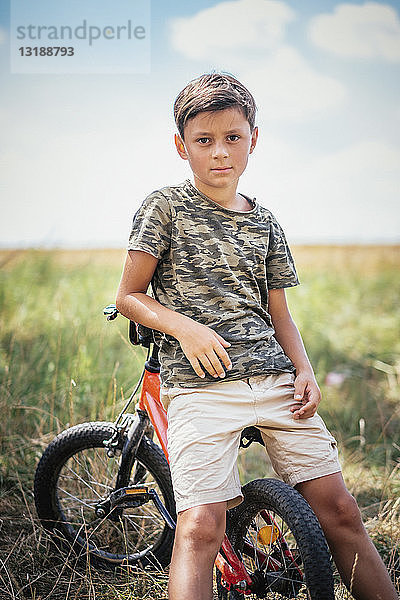 Porträt ernster Junge auf Fahrrad in Feld