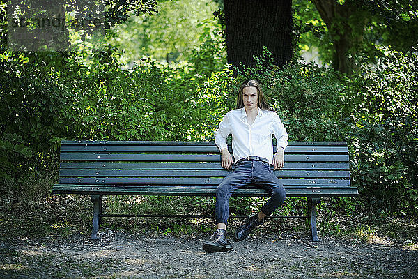 Porträt selbstbewusster junger Mann auf einer Parkbank sitzend