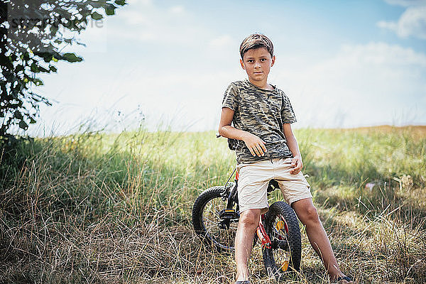 Porträt selbstbewusster Junge auf Fahrrad in ländlichem Gebiet