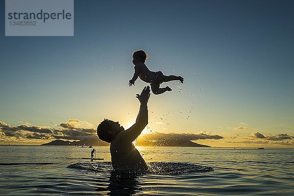 Vater spielt mit seinem kleinen Baby im Wasser bei Sonnenuntergang  Papeete  Tahiti