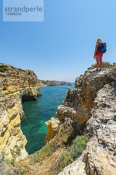 Junge Frau steht auf Felsen an Steilküste  Blick über türkisfarbenes Meer  Strand Praia da Marinha  zerklüftete Felsküste aus Sandstein  Felsformationen im Meer  Algarve  Lagos  Portugal  Europa