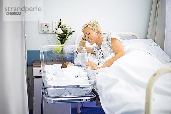 Eine Mutter betrachtet liebevoll ihr neugeborenes Kind  das noch im Krankenhaus liegt
