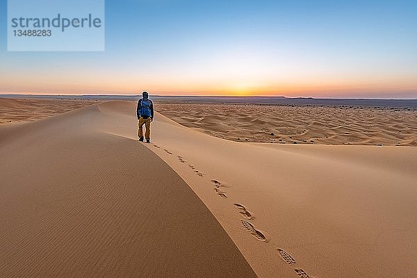 Junger Mann auf einer Sanddüne bei Sonnenaufgang  Erg Chebbi  Merzouga  Sahara  Marokko  Afrika