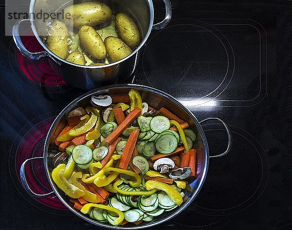 Frisch geschnittenes Gemüse  Karotten  Paprika  Champignons und Auberginen in einer Pfanne und kochende Pellkartoffeln auf roten Kochplatten  Deutschland  Europa