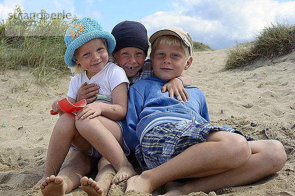 Drei kleine Kinder sitzen zusammen am Strand  Bretagne  Frankreich  Europa