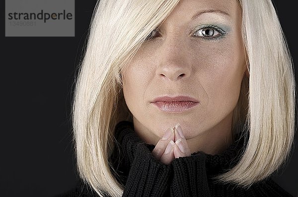 Porträt einer jungen blonden Frau in einem schwarzen Pullover  die Hände zum Gebet gefaltet