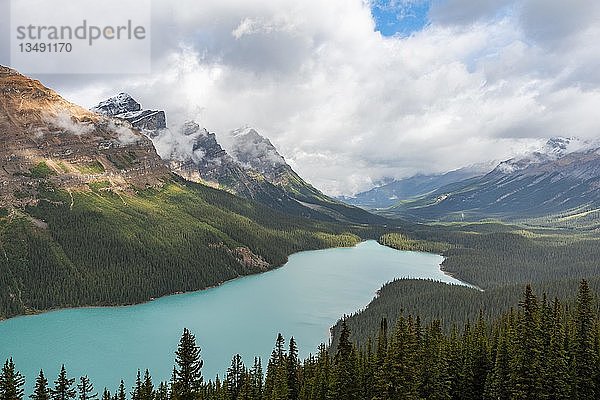 Wolken hängen in Bergspitzen  türkisfarbener Gletschersee umgeben von Wald  Peyto Lake  Rocky Mountains  Banff National Park  Provinz Alberta  Kanada  Nordamerika