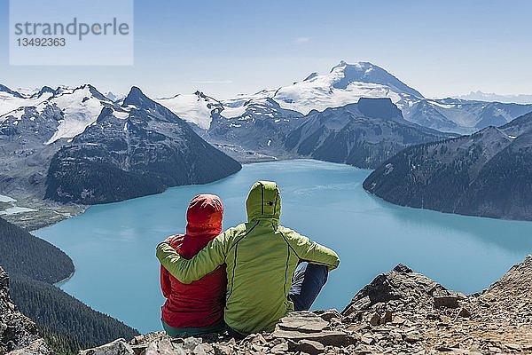 Blick vom Panorama Ridge Trail  Zwei Wanderer sitzen auf einem Felsen mit Garibaldi Lake  türkisfarbener Gletschersee  Guard Mountain und Deception Peak  Gletscher  Garibaldi Provincial Park  British Columbia  Kanada  Nordamerika