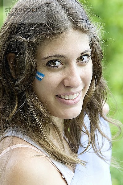 Porträt einer jungen Argentinierin mit der argentinischen Flagge auf der Wange