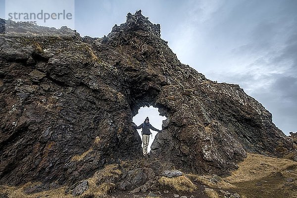 Junger Mann steht in einem Felsbogen  vulkanisches Gestein am Strand von Djúpalónssandur  Halbinsel Snæfellsnes  Westisland  Island  Europa
