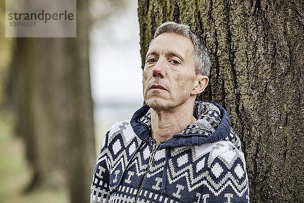 Mann  grauhaarig lehnt an einem Baum und schaut in die Kamera  Köln  Nordrhein-Westfalen  Deutschland  Europa