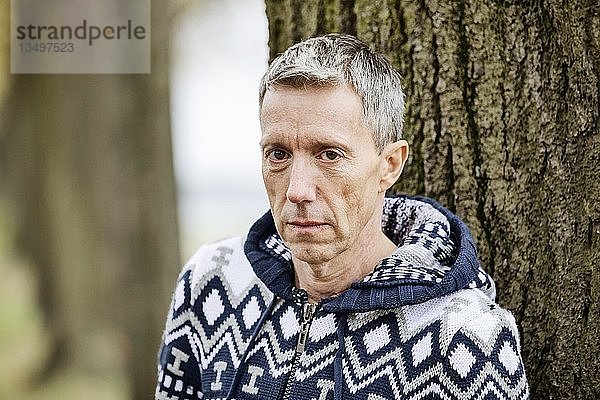 Mann  grauhaarig  lehnt an einem Baum und schaut in die Kamera  Köln  Nordrhein-Westfalen  Deutschland  Europa