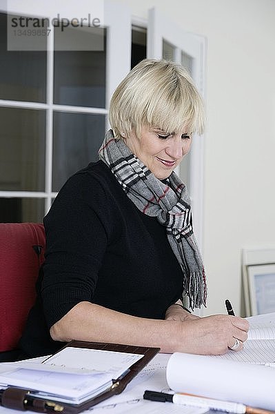 Eine Architektin sitzt an ihrem Schreibtisch in ihrem Büro und schreibt