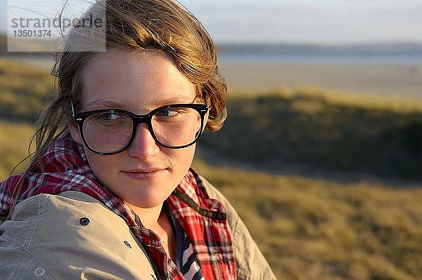Eine junge Frau mit großer schwarzer Brille sitzt auf einer Düne  Bretagne  Frankreich  Europa