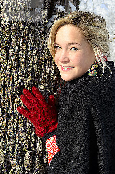 Junge Frau lehnt im Winter an einem Baum