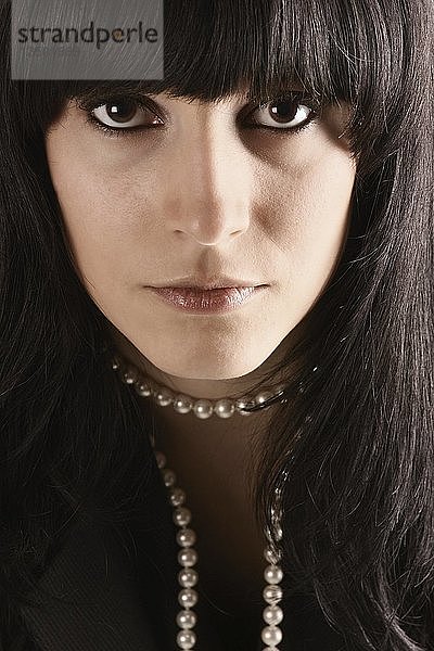 Porträt eines Mädchens mit schwarzen Haaren und braunen Augen  das eine Perlenkette trägt