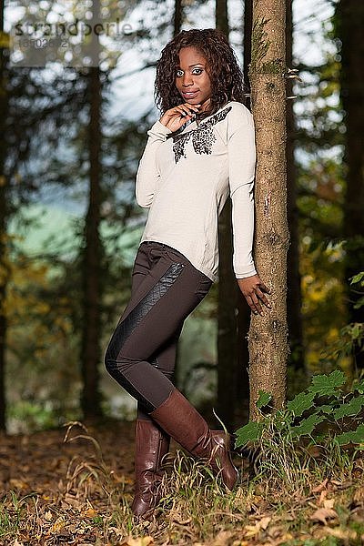 Dunkelhäutige junge Frau im Herbstoutfit im Wald