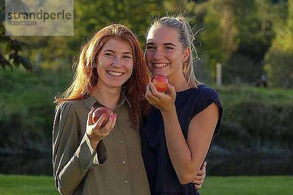 Zwei Mädchen  junge Frauen  lachend Äpfel essend  im Garten  Oberbayern  Bayern  Deutschland  Europa