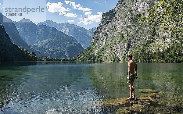 Junger Mann steht auf einem Stein im Obersee  hinter dem Watzmannmassiv  Salet am Königssee  Nationalpark Berchtesgaden  Berchtesgadener Land  Oberbayern  Bayern  Deutschland  Europa