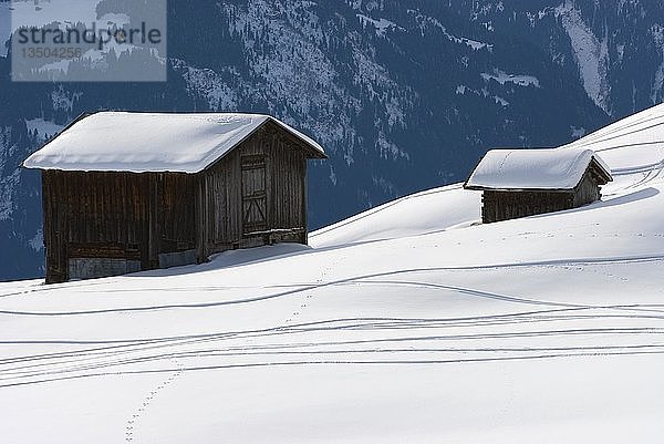 Verschneite Berghütte  die Heu auf einem schneebedeckten Hang mit Skispuren lagert  Graubünden  Schweiz  Europa