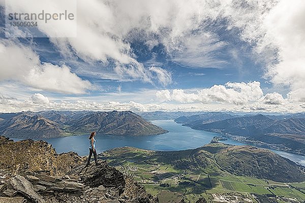 Eine Wanderin steht auf den Felsen in The Remarkables  mit Blick auf den Lake Wakatipu  die Berge und Queenstown  Queenstown  Otago  Südinsel  Neuseeland  Ozeanien