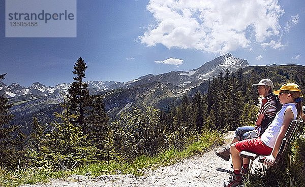 Mutter und Kind sitzen auf einer Bank und genießen den Blick auf die Alpengipfel in der Nähe des Kreuzecks  Partenkirchen  Bayern  Deutschland  Europa