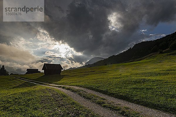 Kleine Hütte auf Bergwiese mit Weg und dramatischem Wolkenhimmel  Gerold  Mittenwald  Bayern  Deutschland  Europa