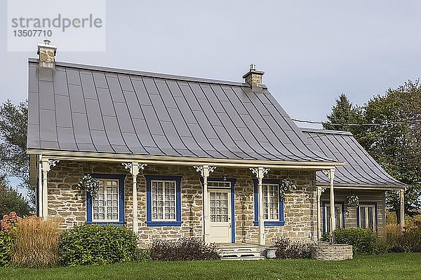 Alte Feldsteinfassade im Landhausstil von 1820 mit blauer Zierleiste und braunem Stehfalz-Blechdach sowie Anbau aus gestapelten Baumstämmen im Herbst  Quebec  Kanada  Nordamerika