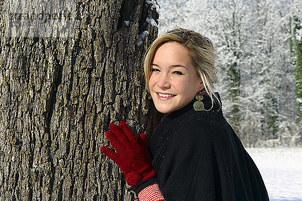 Junge Frau lehnt im Winter an einem Baum