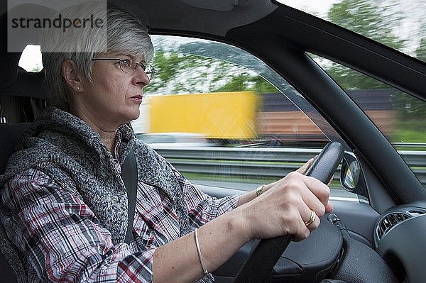 Frau mittleren Alters  über 50 Jahre  am Steuer eines Autos auf einer Autobahn