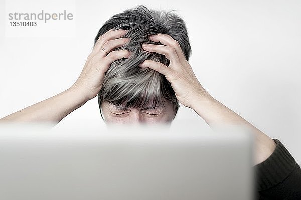 Gestresste Frau  die hinter einem Computerbildschirm sitzt und an ihren Haaren zieht