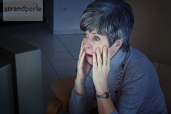 Frau  die vor ihrem Fernseher sitzt und schockiert die Nachrichten verfolgt