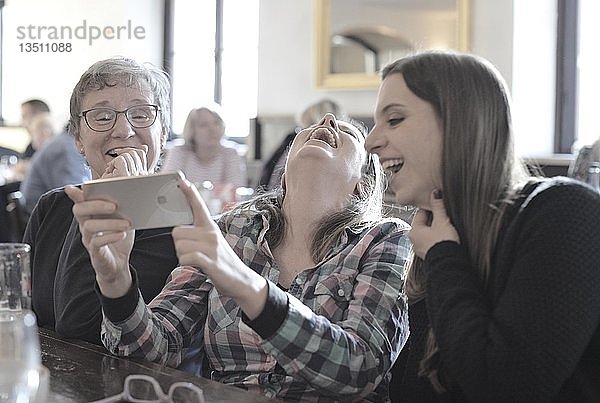 Junge Frauen und ältere Frauen betrachten Smartphone  Lachen  Porträt  Café  Stuttgart  Baden-Württemberg  Deutschland  Europa