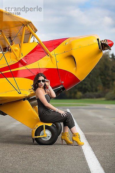 Junge Frau mit Sonnenbrille in Overall und Stiefeln posiert vor einem Doppeldecker-Flugzeug  Mode  Lifestyle  Fotoshooting