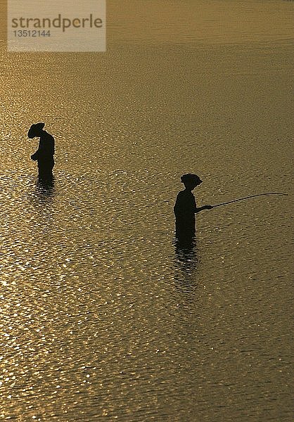 Silhouetten von Fischern  die bei Sonnenuntergang im Wasser stehen
