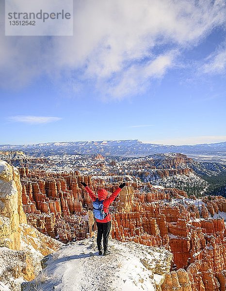 Junge Frau mit ausgestreckten Armen mit Blick auf das Amphitheater  bizarre schneebedeckte Felslandschaft mit Hoodoos im Winter  Rim Trail  Bryce Canyon National Park  Utah  USA  Nordamerika