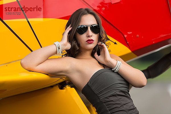 Junge Frau mit Sonnenbrille in Overall und Stiefeln posiert vor einem Doppeldecker-Flugzeug  Mode  Lifestyle  Fotoshooting