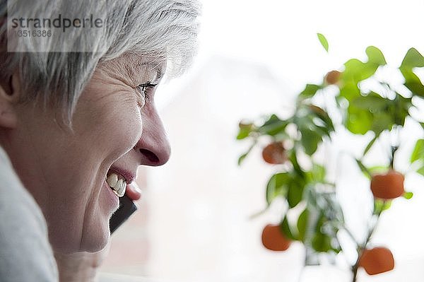 Frau  50+  schaut aus dem Fenster während sie telefoniert