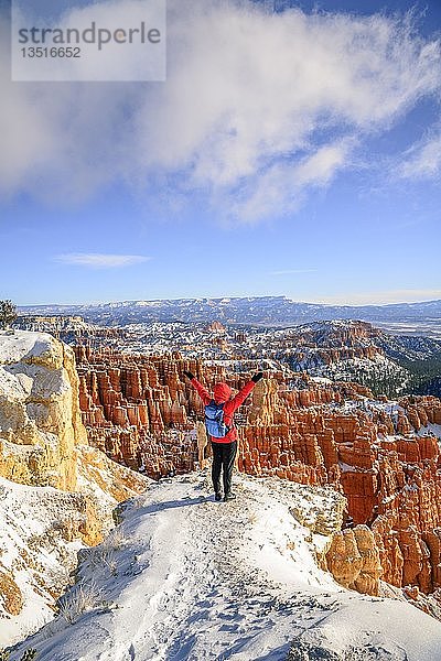 Junge Frau mit ausgestreckten Armen und Blick auf das Amphitheater  bizarre verschneite Felslandschaft mit Hoodoos im Winter  Rim Trail  Bryce Canyon National Park  Utah  USA  Nordamerika