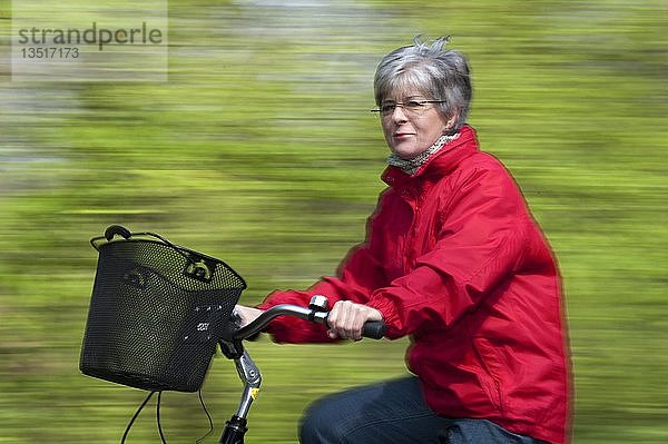 Ältere Frau in roter Jacke auf dem Fahrrad