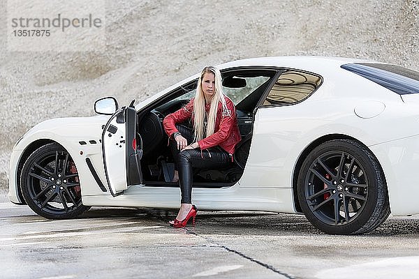 Junge Frau mit langen blonden Haaren posiert mit weißem Maserati Gran Turismo MC Stradale