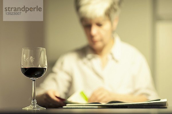 Frau  die am Tisch sitzt und eine Zeitung liest  mit einem Glas Rotwein vor sich