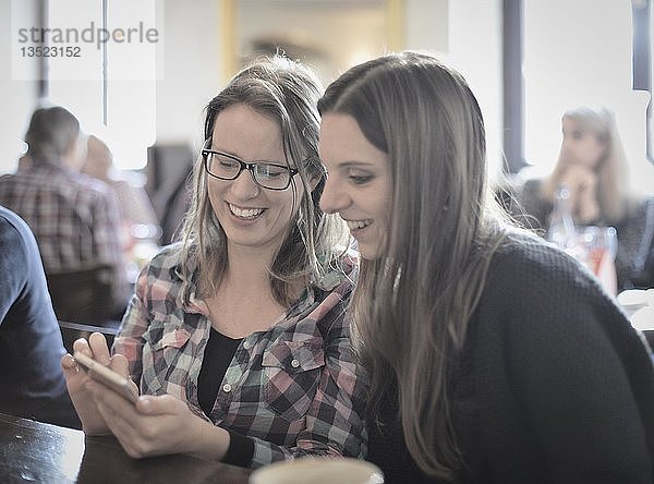 Junge Frauen schauen auf Smartphones und lachen  Portrait  Café  Stuttgart  Baden-Württemberg  Deutschland  Europa