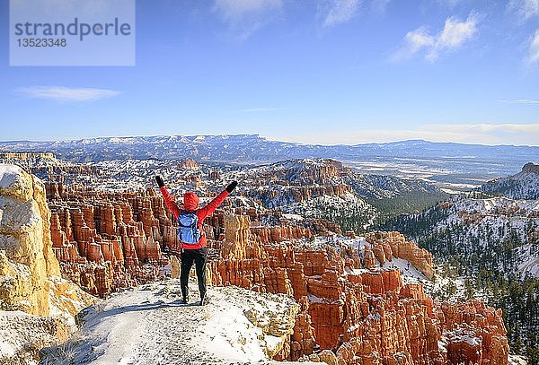 Junge Frau mit ausgestreckten Armen und Blick auf das Amphitheater  bizarre verschneite Felslandschaft mit Hoodoos im Winter  Rim Trail  Bryce Canyon National Park  Utah  USA  Nordamerika