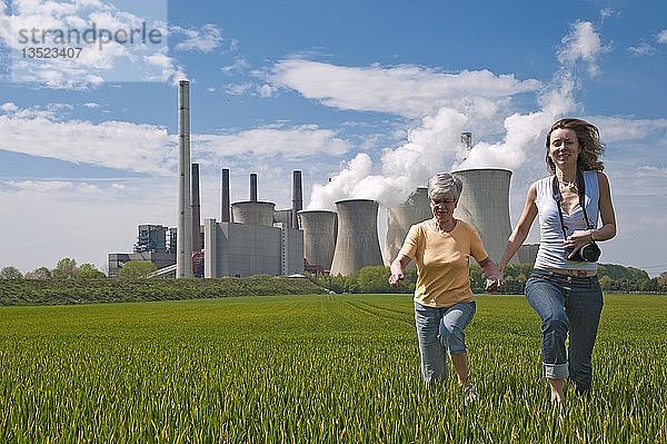 Zwei Frauen laufen durch ein Feld vor dem Kraftwerk Neurath  Grevenbroich  Rheinland  Nordrhein-Westfalen  Deutschland  Europa